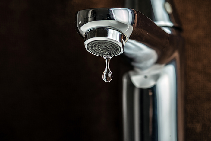 A drop of pure water dripping from the tap. On a dark background. Selective focus.