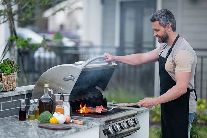 Male chef grilling and barbecuing in garden. Barbecue outdoor garden party. Handsome man preparing barbecue meat. Concept of eating and cooking outdoor during summer time