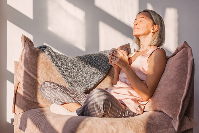 Adult woman sitting on the sofa at home and having a cup of coffee, relaxation concept