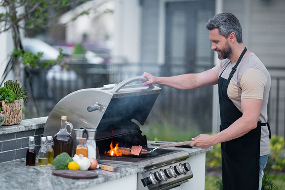 Man grilling fish outside with cooking ingredients by his side on counter