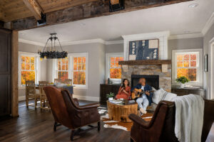 Man and woman sitting in living room next to fireplace with Renewal by Andersen Windows in the background