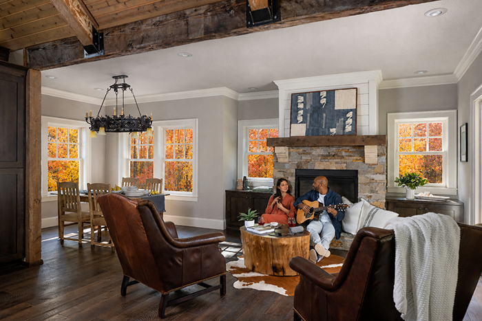 Man and woman sitting in living room next to fireplace with Renewal by Andersen Windows in the background